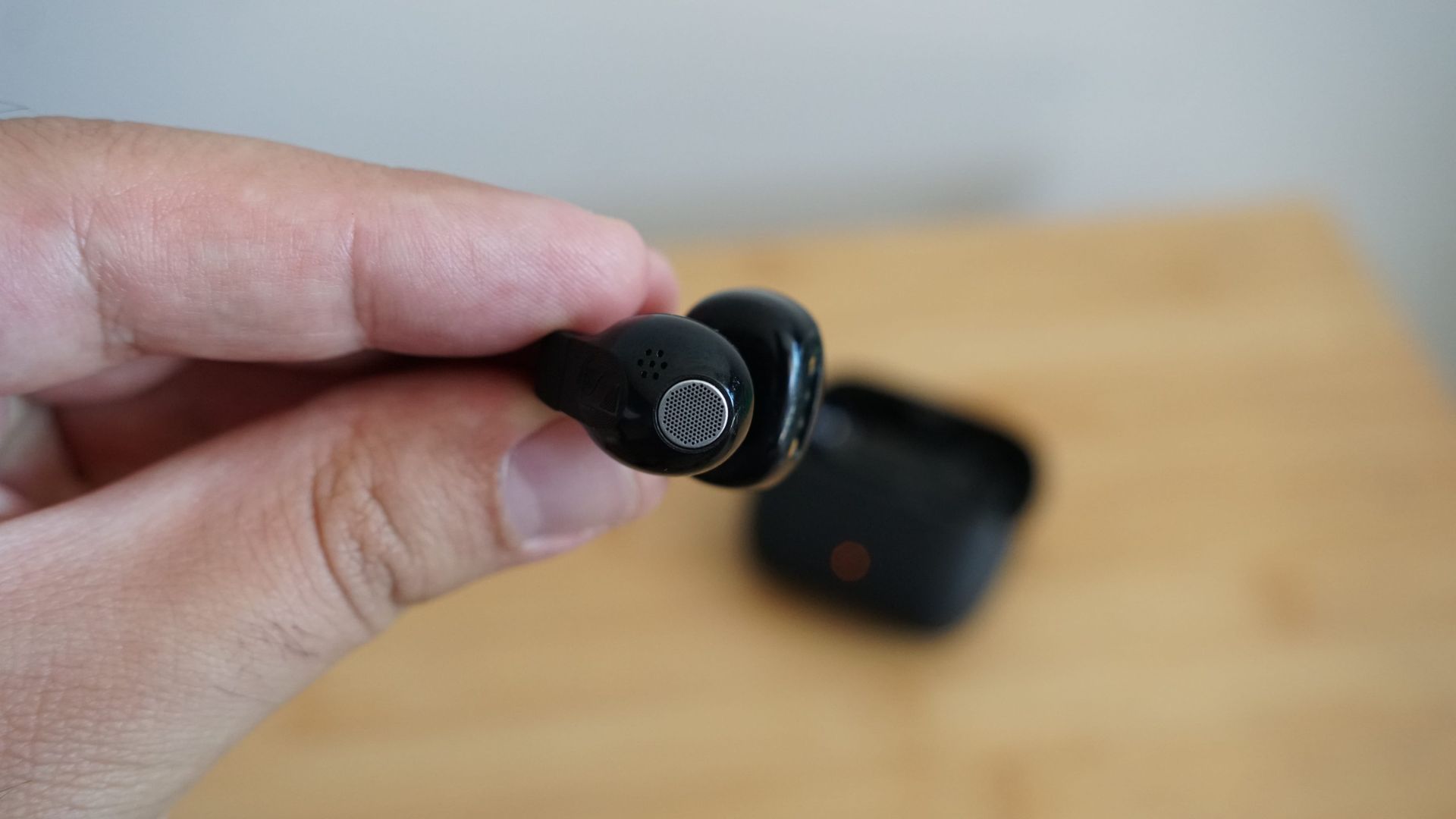 Sennheiser's Accentum Clip held in a hand, over a wooden table, with the case visible