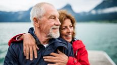 Senior couple tourist standing by lake in nature on holiday, hugging.