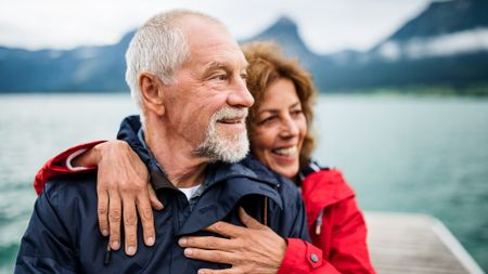 Senior couple tourist standing by lake in nature on holiday, hugging.
