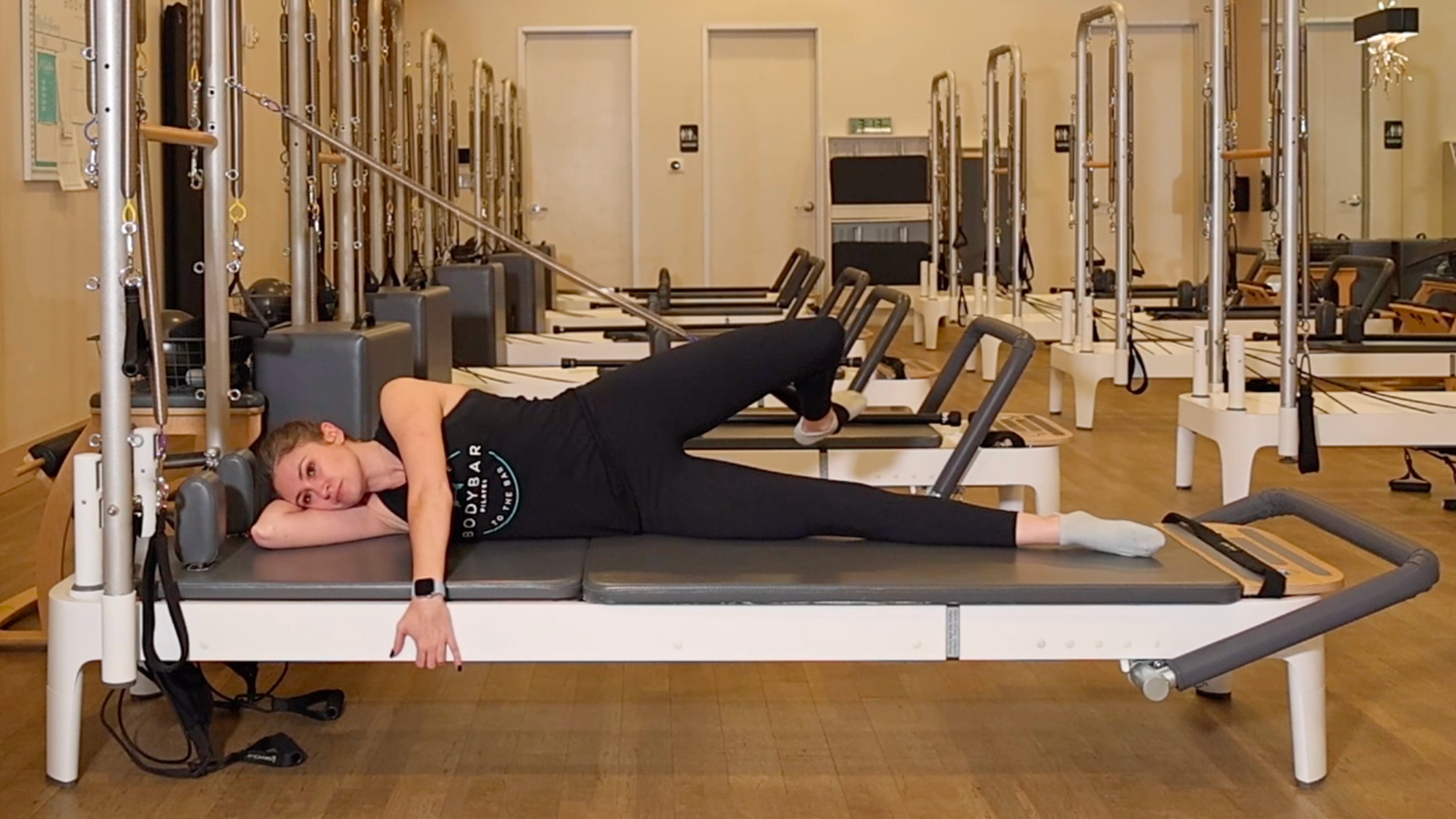 Woman demonstrating a Pilates exercise on the carriage of a Pilates reformer machine