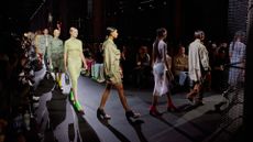 Miu Miu S/S 2023. Female models wearing various types of dresses walking down a runway with people sitting next to it.