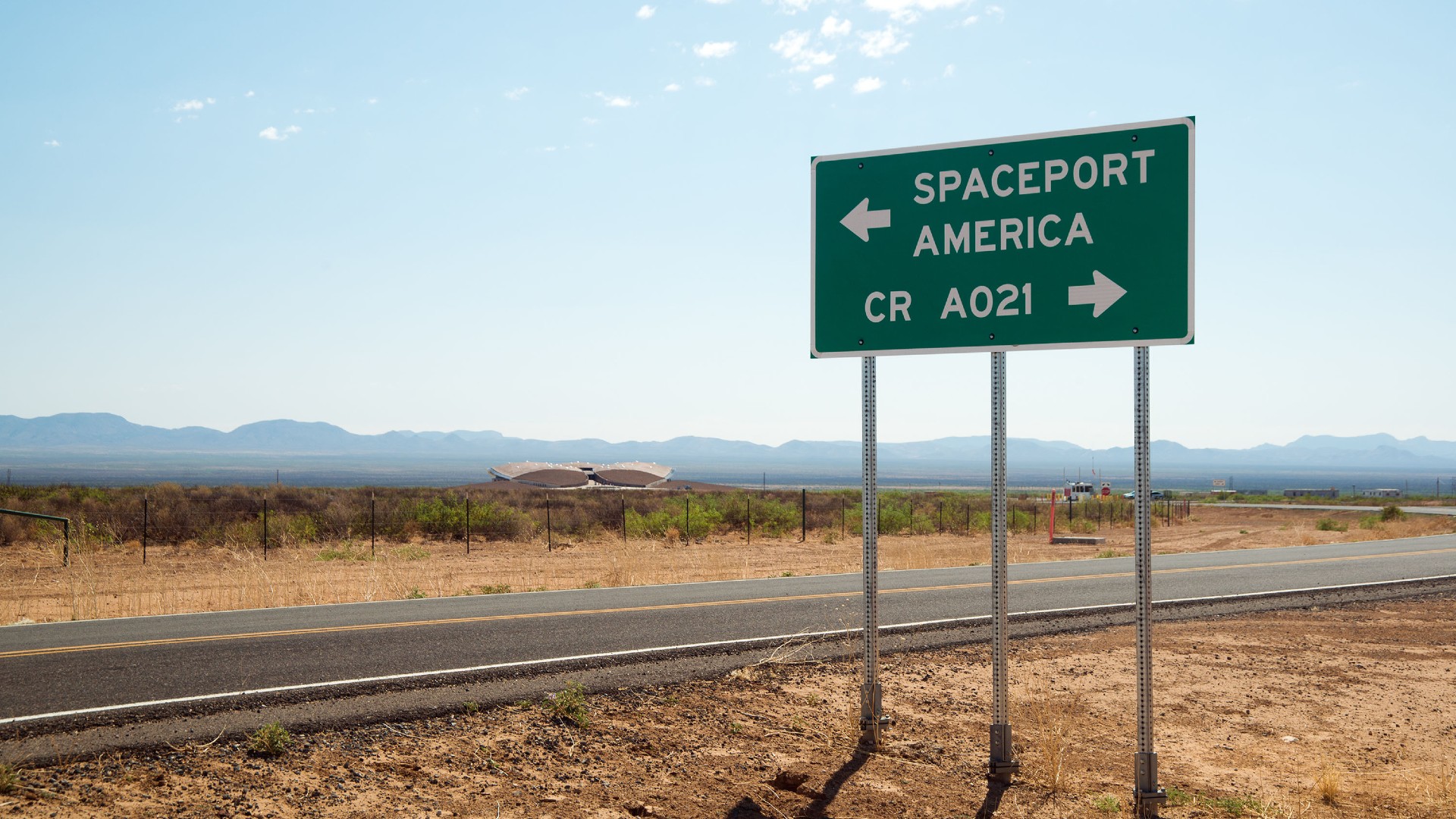 a sign by a highway in the desert reading "spaceport america" with a sign pointing to the left, and another sign pointing to the right reading "CR A021"