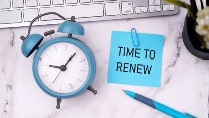 A clock on a desk next to a note that says Time To Renew