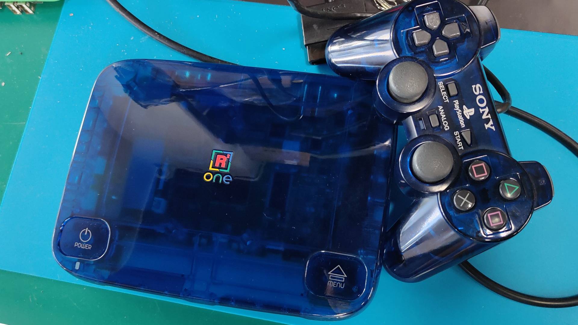 Photo of SuperStation FPGA console in midnight blue next to original DualShock controller.