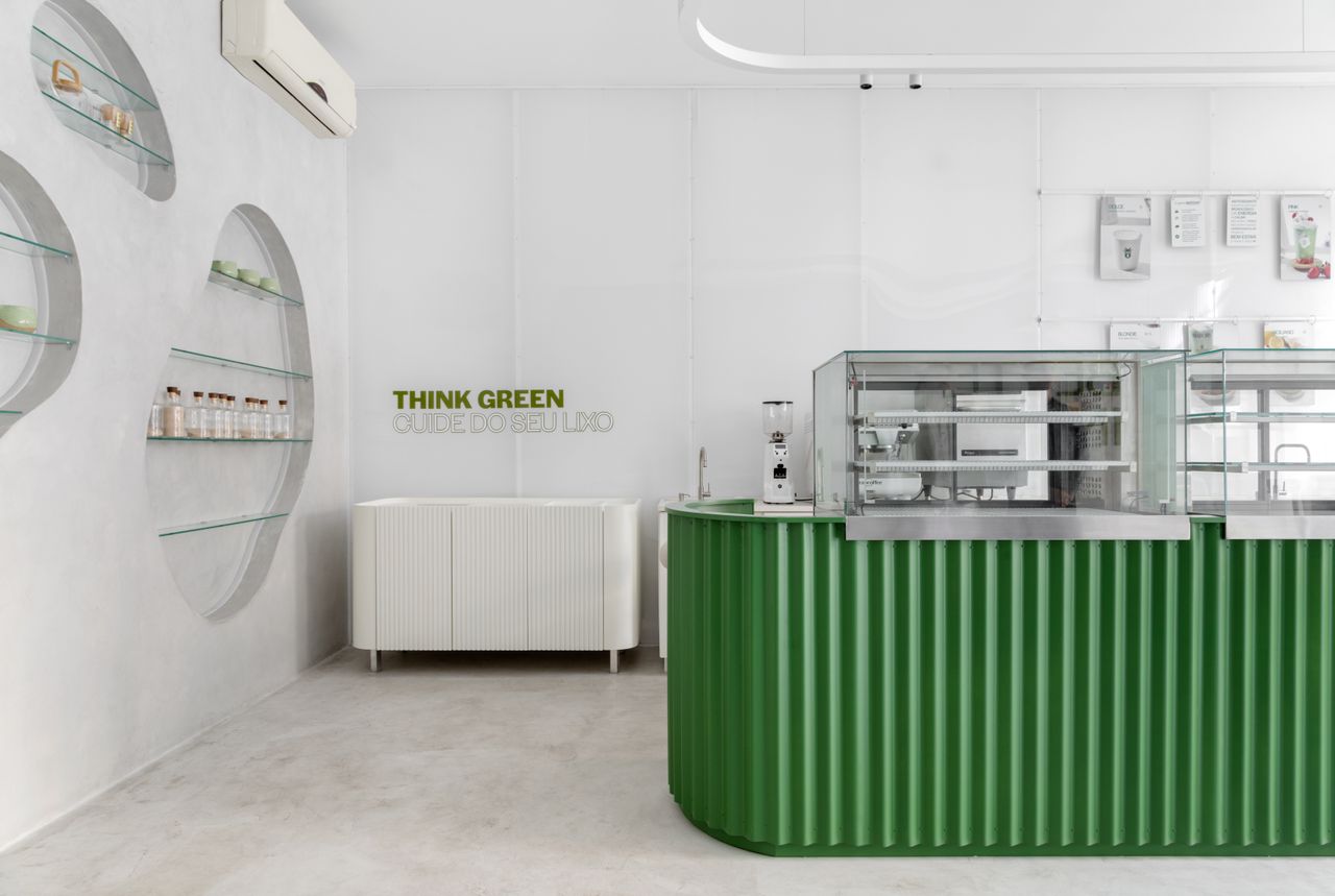 A white-washed, plastered matcha cafe with sculptural decor features monochromatic furnishings and an emerald green and chrome bar counter.
