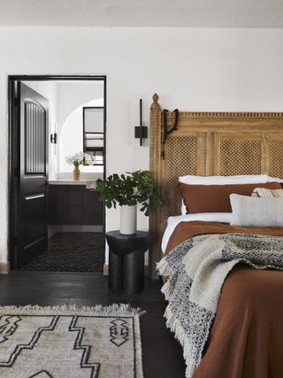 bedroom in meditterranean style house with black wood floors, white walls, vintage wooden headboard and white and terracotta bedding