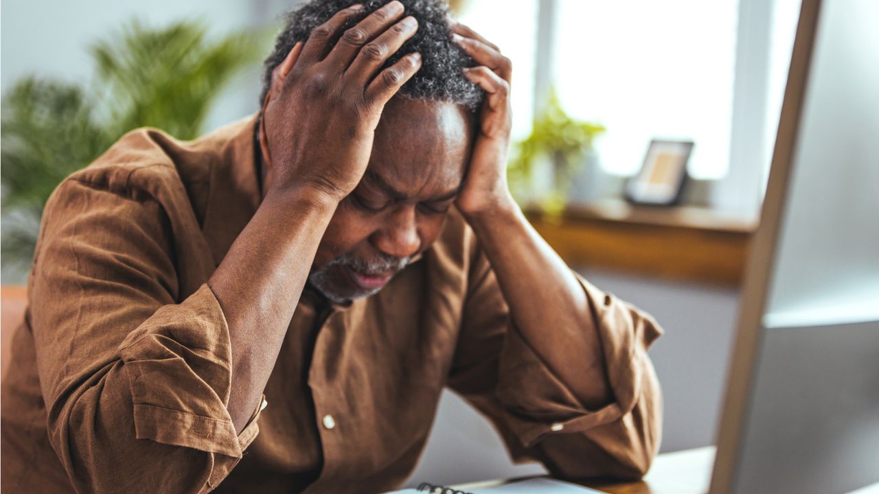 A man sits with his head in his hands and his elbows on a table, clearly upset.