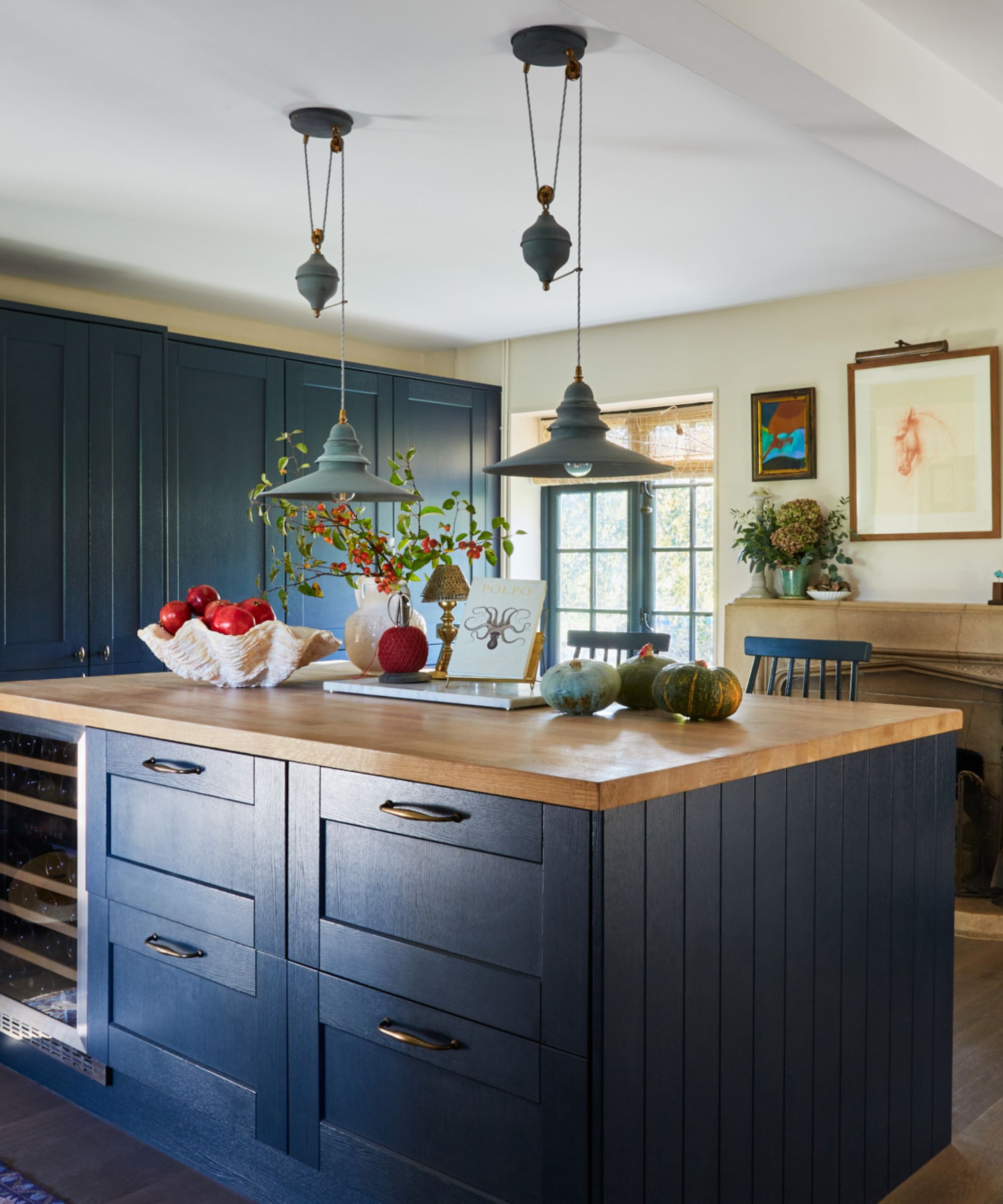 A blue kitchen with a large island topped with a lamp
