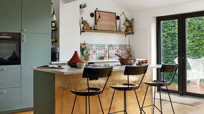 wooden kitchen flooring, green and gold island unit with brown stools