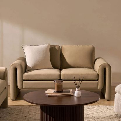 Latte coloured two seater sofa with a cream cushion and wooden coffee table in front