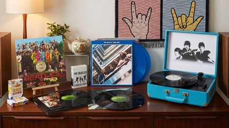 Seveal Beatles vinyl albums on a wooden sideboard, with a Beatles-branded suitcase turntable, plus some Beatles playing cards and A Hard Day's Night on Blu-ray