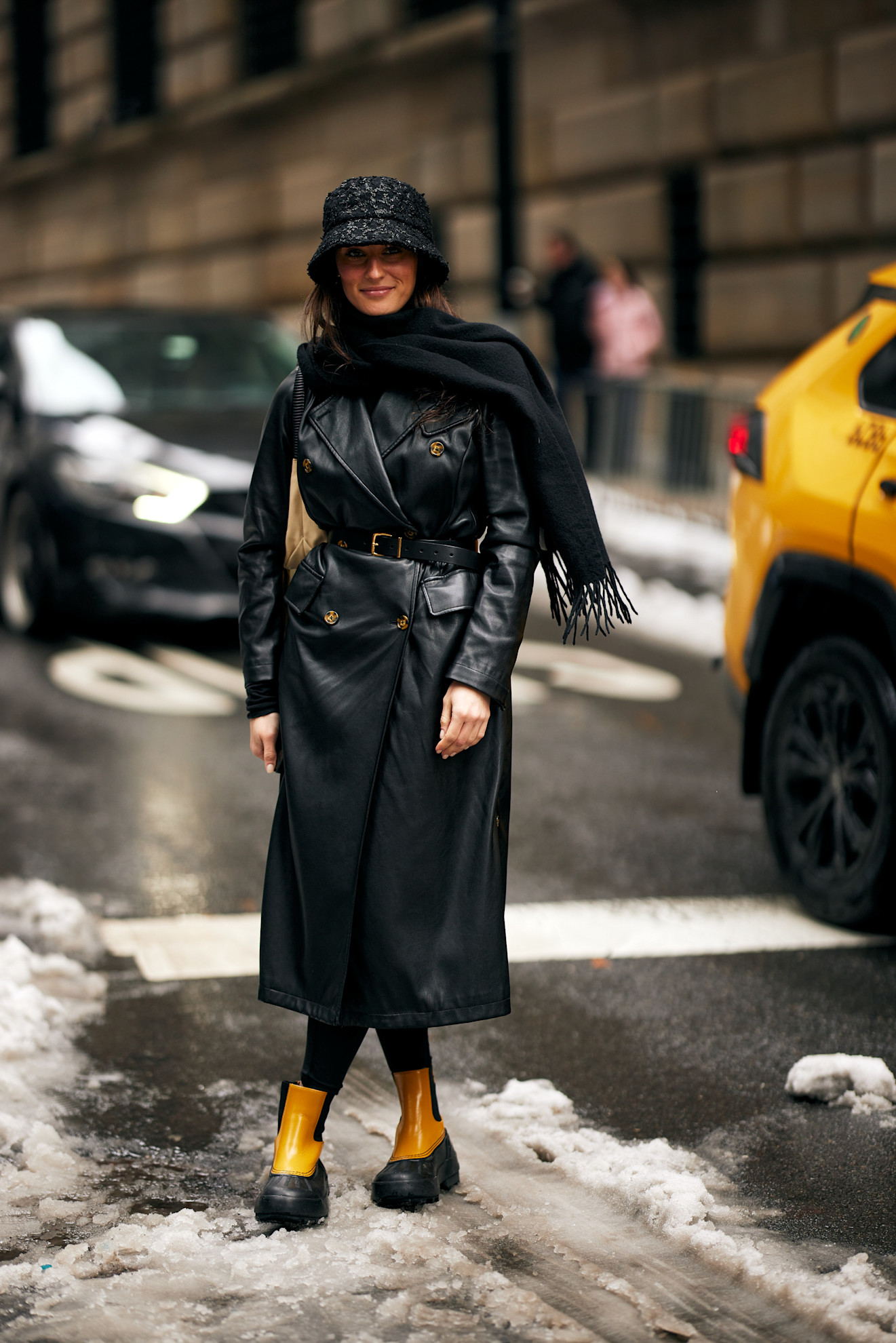 a woman in a black leather coat, tights, scarf, hat, and yellow Chelsea boots at new york city fashion week.