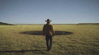 A lone cowboy walks towards a hole