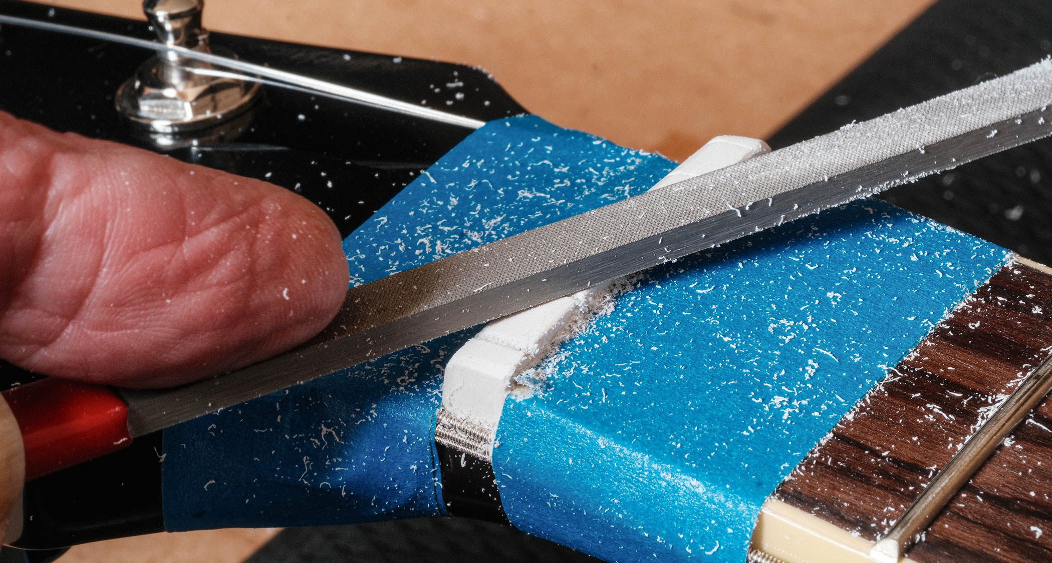 A guitar's nut is being filed to smooth it off.