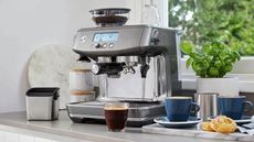 One of the best best coffee makers with grinders, Breville The Barista Pro on a kitchen countertop with a croissant and coffee around it