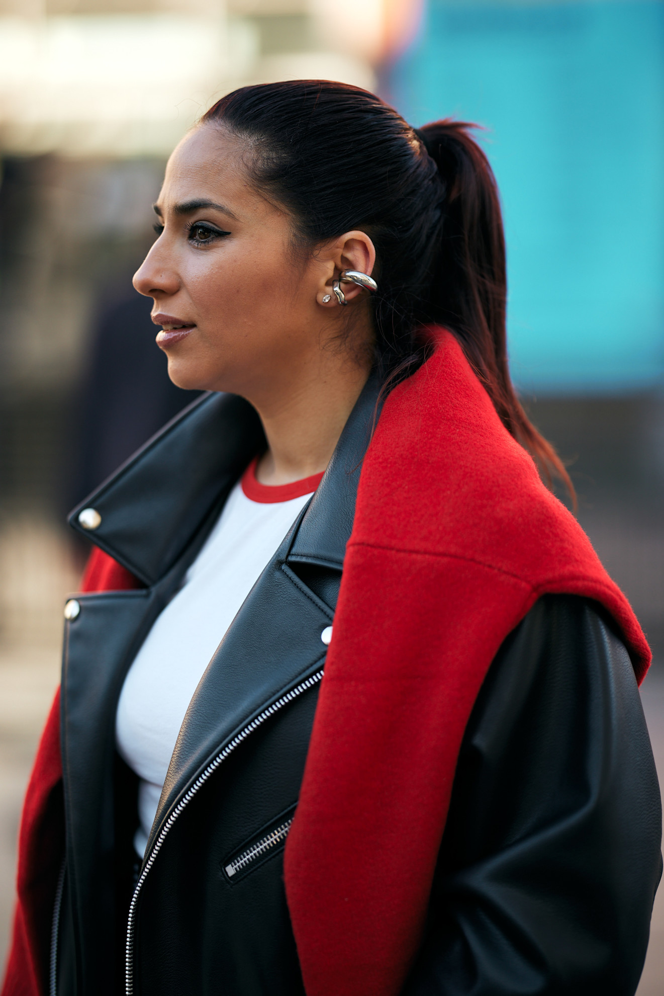 a woman with a brunette ponytail wearing a black leather jacket and a red sweater over her shoulders