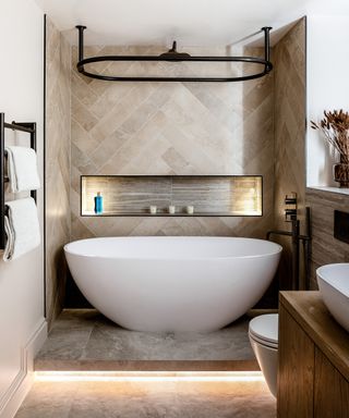 A bathroom with neutral stone tiles and freestanding white tub