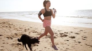 A woman jogging on the beach alongside one of the best dogs for runners 