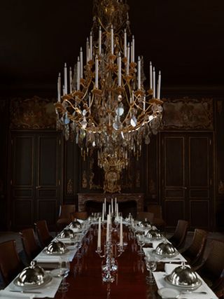 A wood-panelled dining room with a long dining table below a chandelier