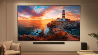 A wall-mounted LG QNED evo TV displaying a lighthouse at sunset. The TV is staged in a modern living room alongside a soundbar and a chair.
