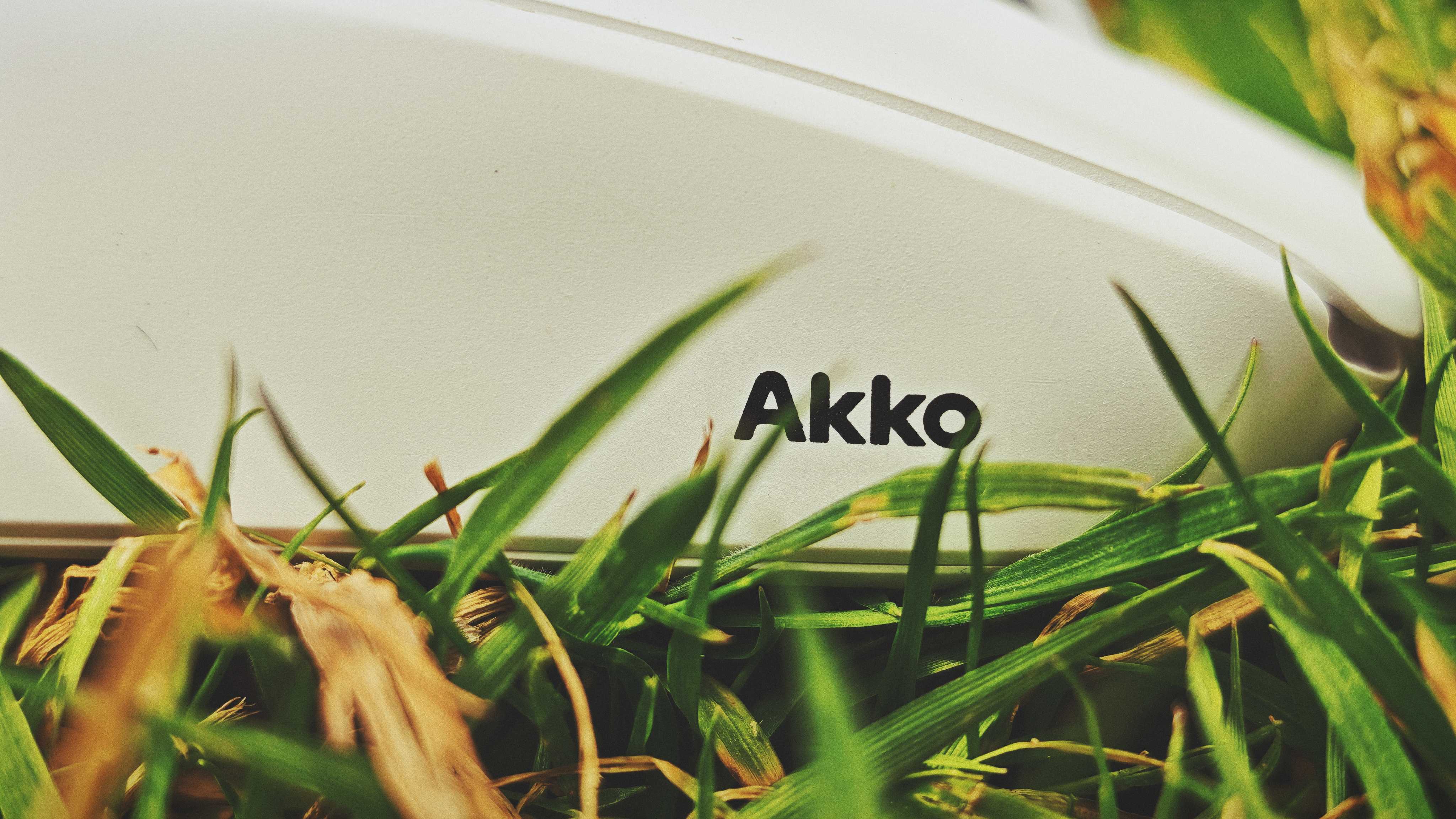 A white and purple Akko Dash Ultra gaming mouse sitting in tall grass in a garden