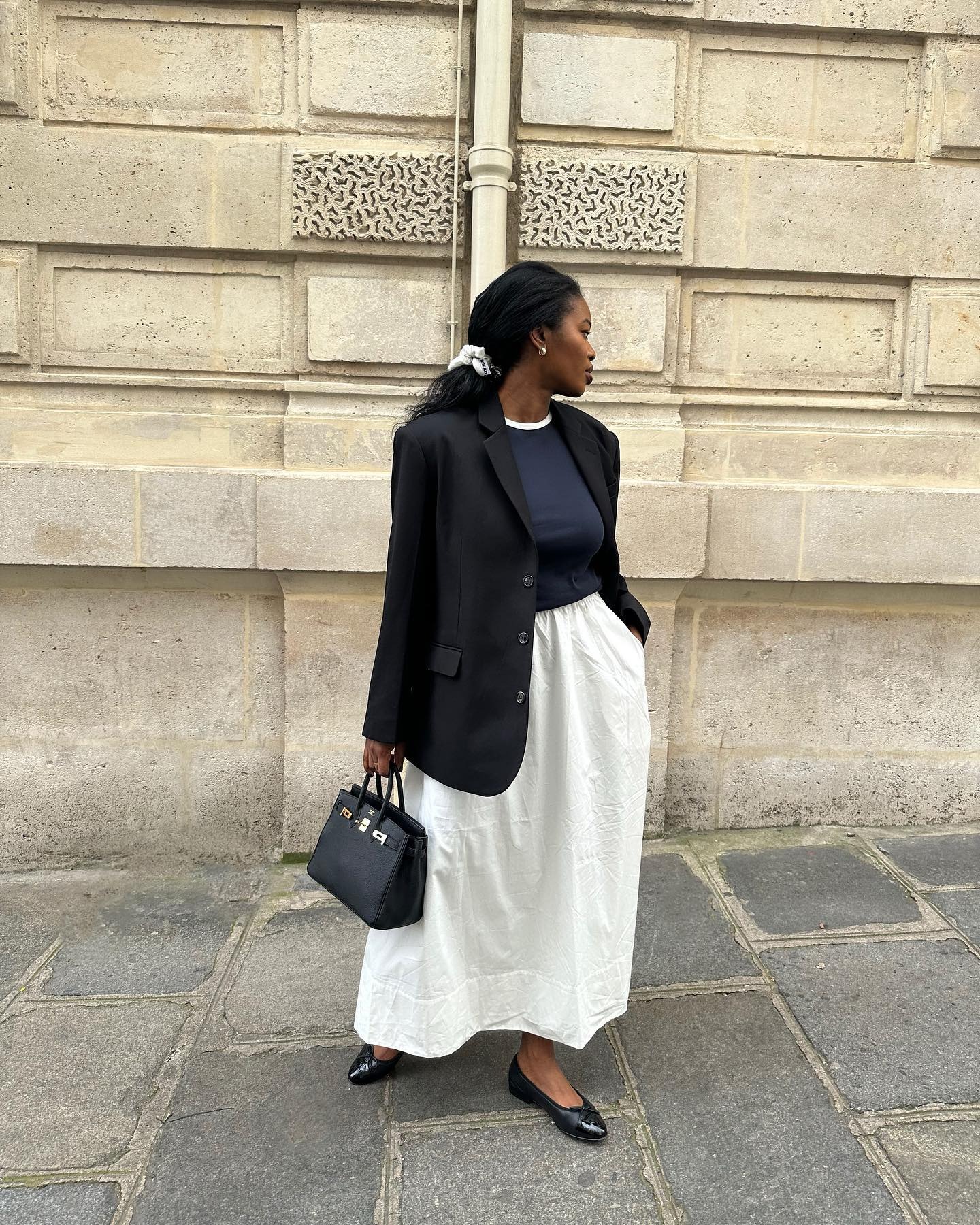 French woman wearing a white maxi skirt, navy T-shirt, black blazer and black heels.