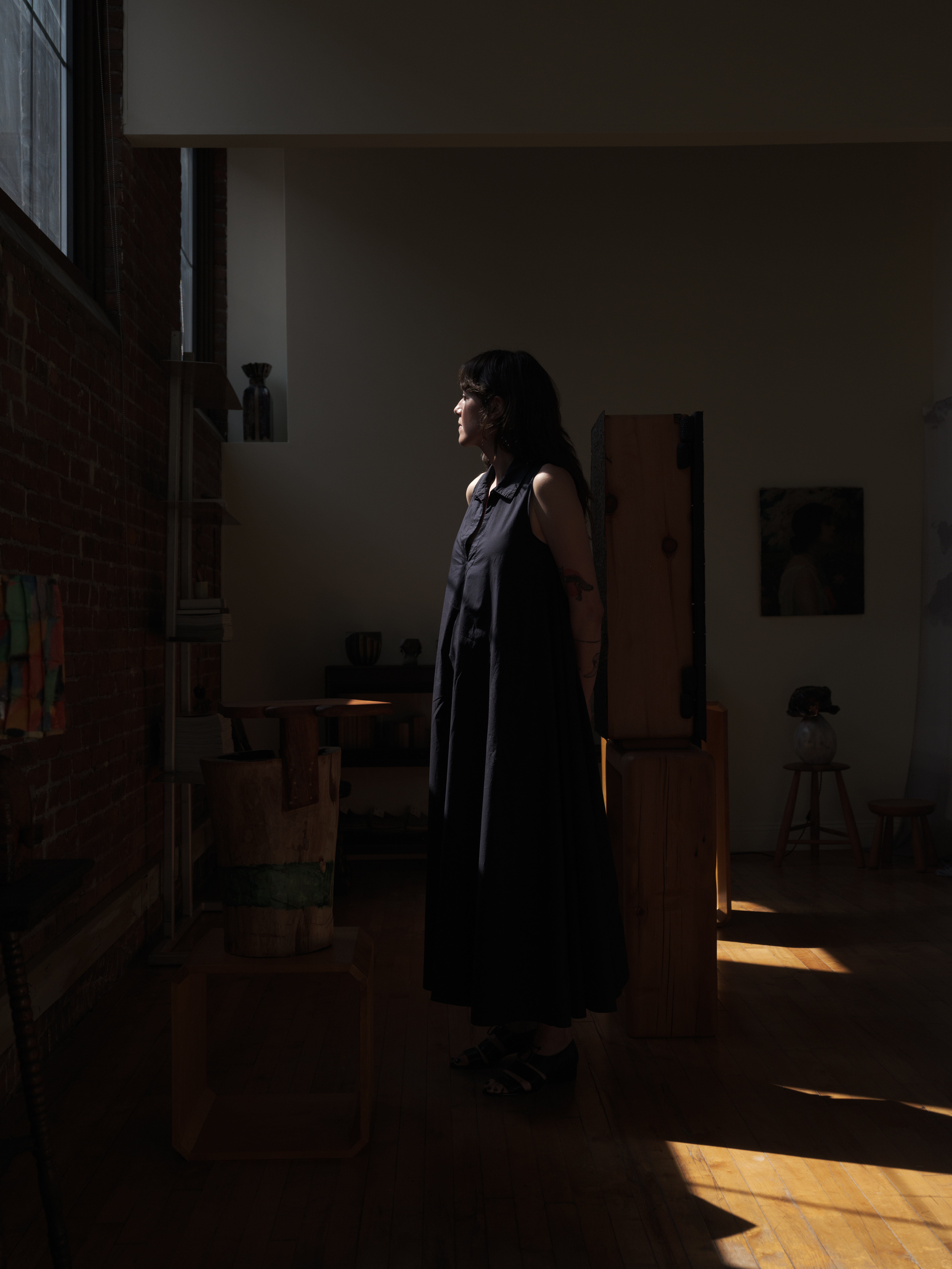 A young woman dressed in a black maxi dress is captured in the shadows in a sun-lit gallery.