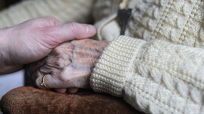 A woman holds the hand of an elderly Alzheimer's patient.