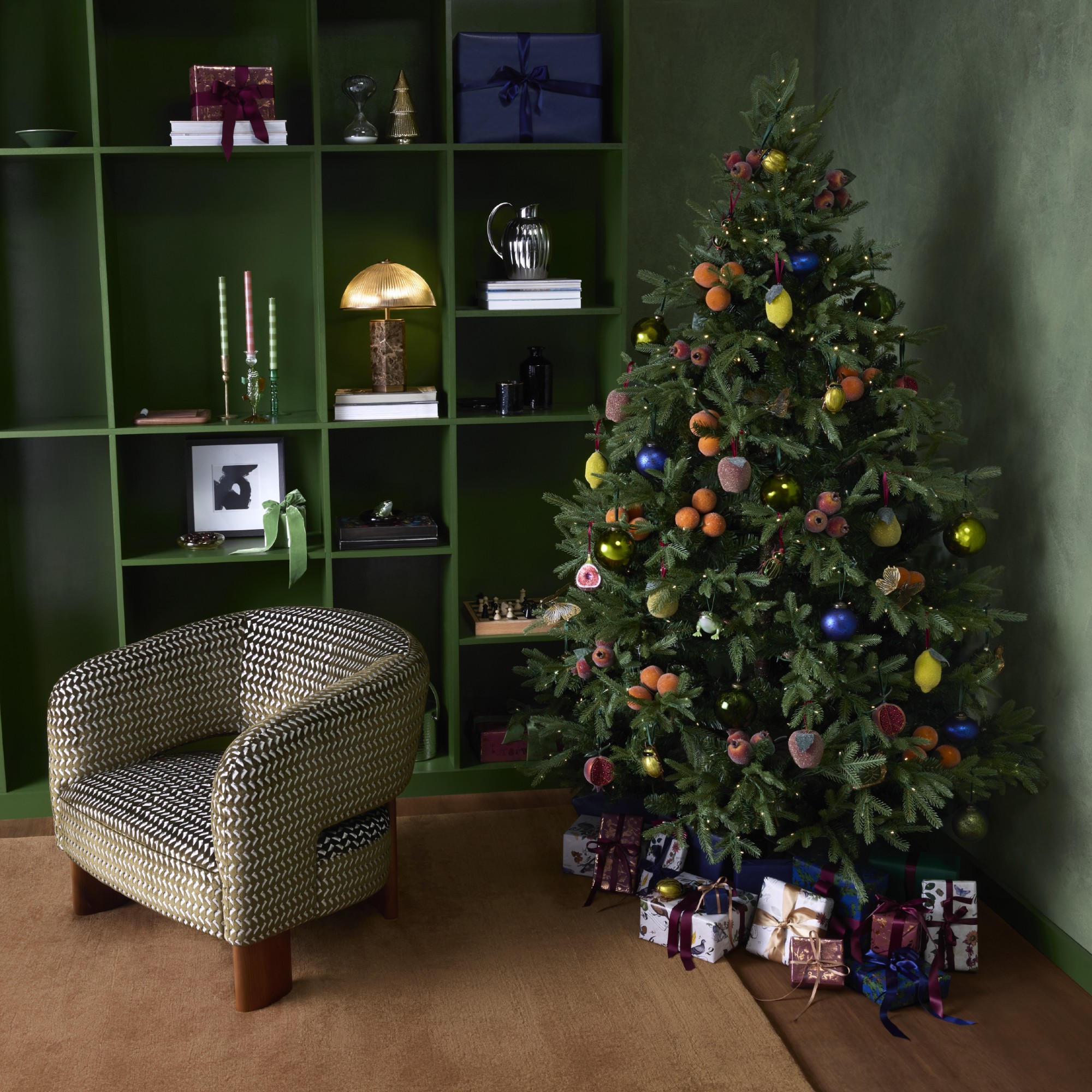 A green-painted room with green bookshelves with a Christmas tree next to it decorated with baubles from the Curator theme at John Lewis.