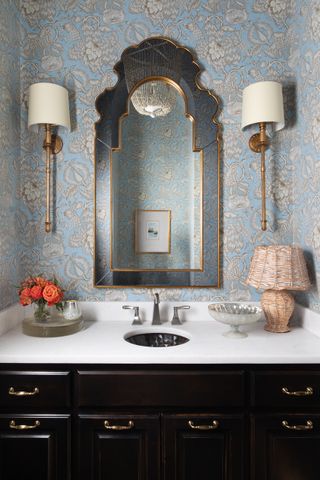 bathroom with black cabinets, gold handles, blue patterned wallpaper and wall scones