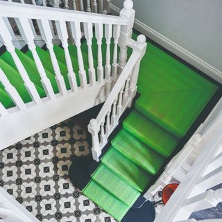 A black staircase with white bannisters and a bright green striped stair runner rug