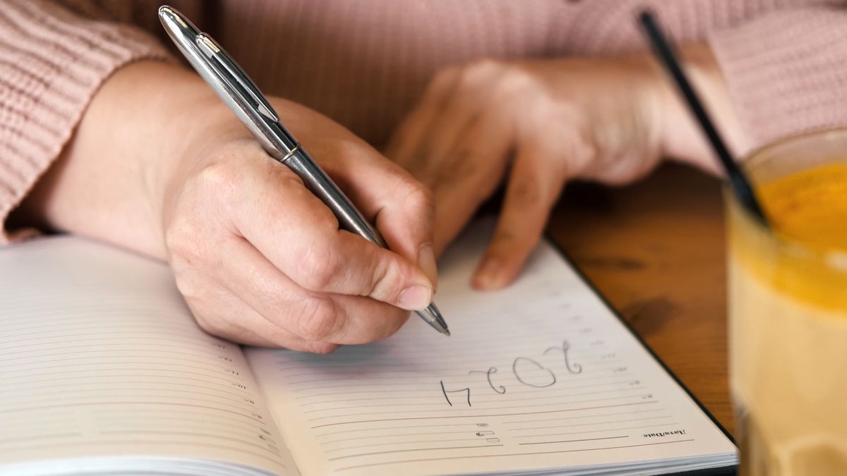 Close-up of hands writing in diary under &quot;2024&quot;