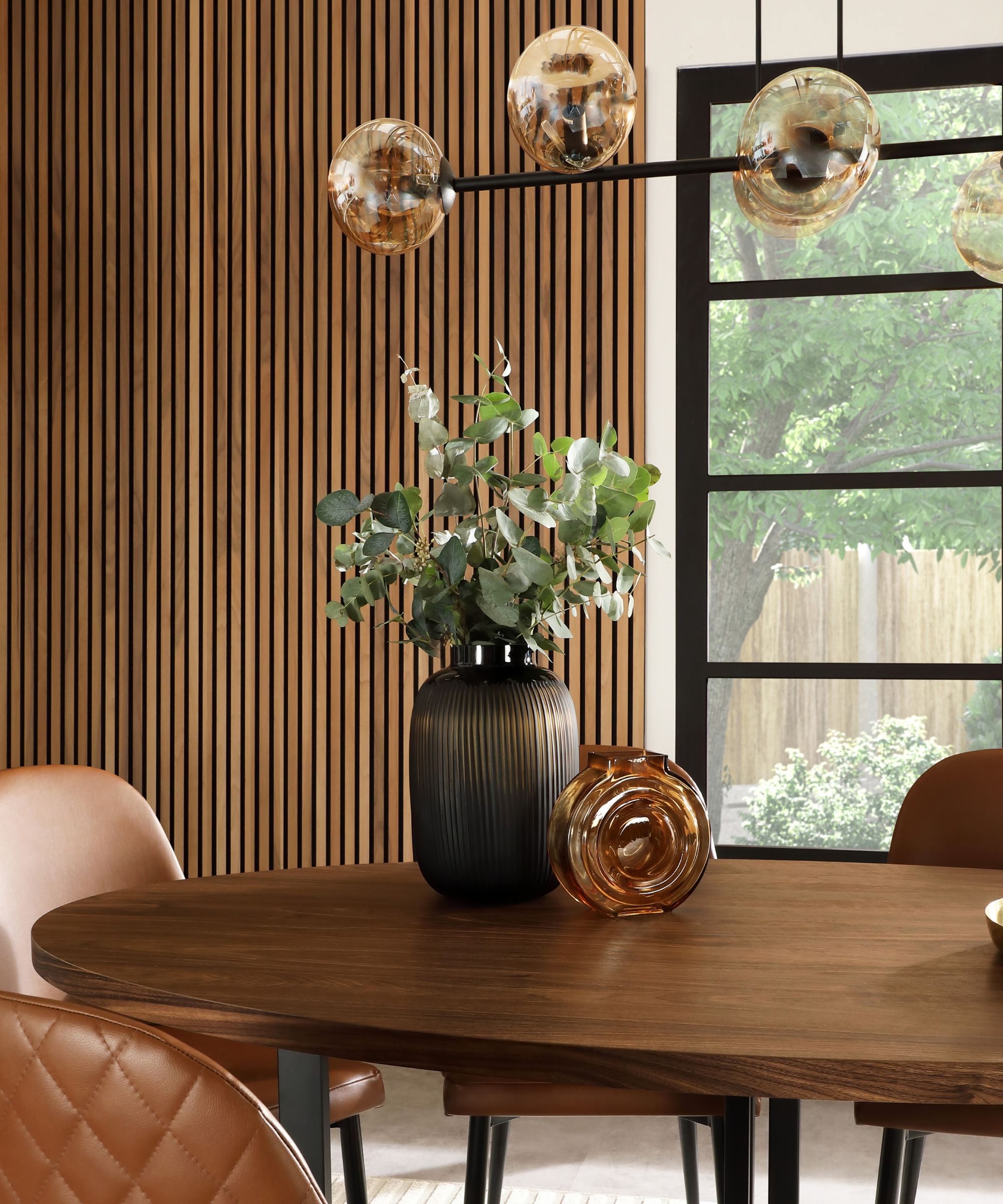 Glass globe pendant light above wooden table with dark ribbed vase and amber glass vase, eucalyptus stems.