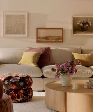 neutral spring decorated living room with a large neutral couch with a small floral footstool and floral wall art