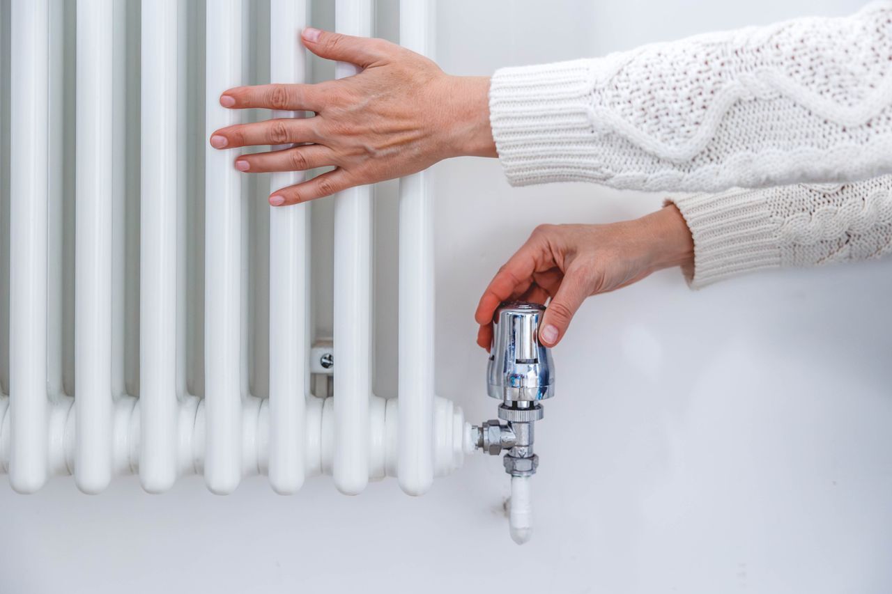 Side shot of woman&#039;s hands in a jumper adjusting the thermostat valve on a heating radiator at home