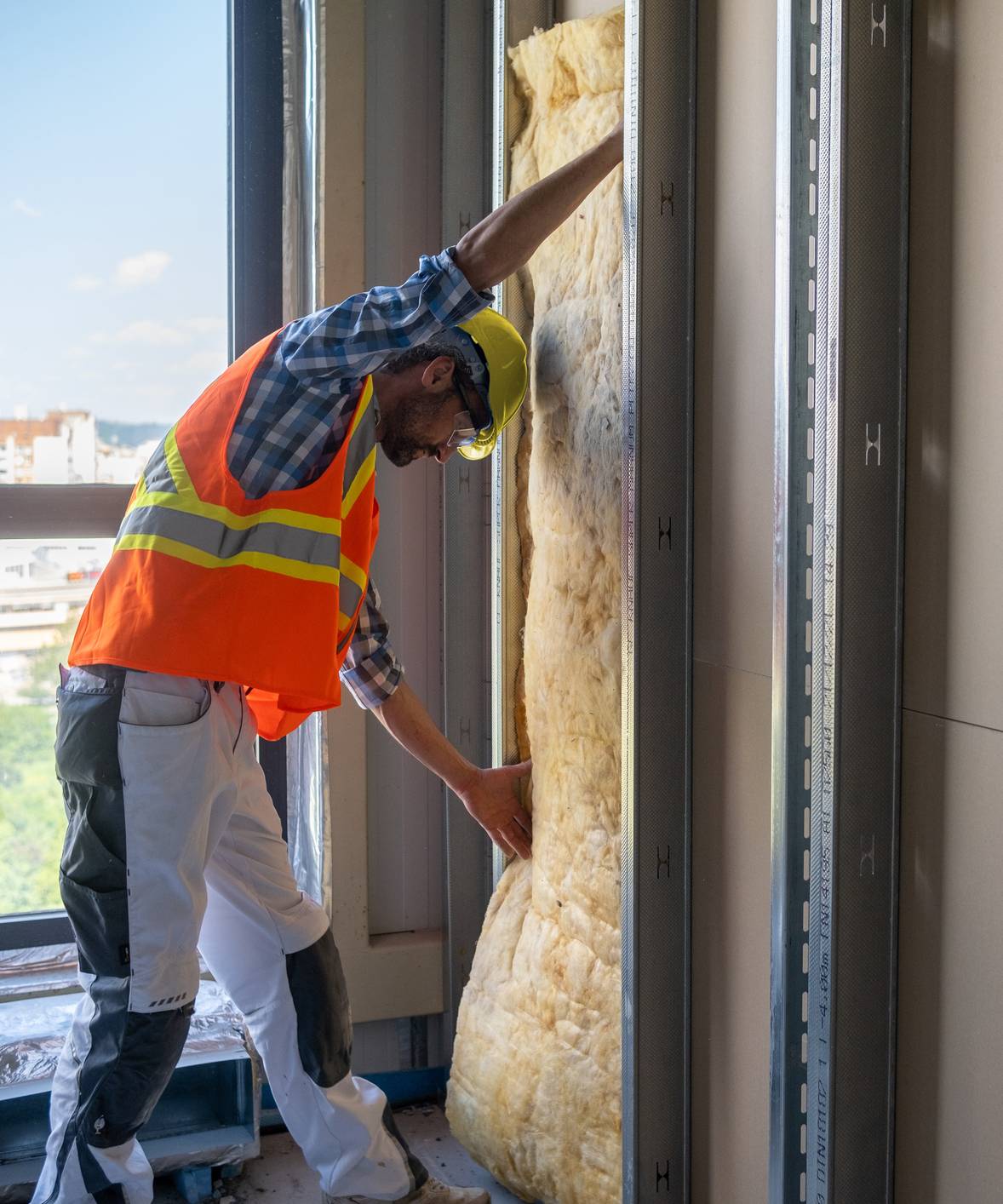 A construction worker installs mineral wool wall insulation.