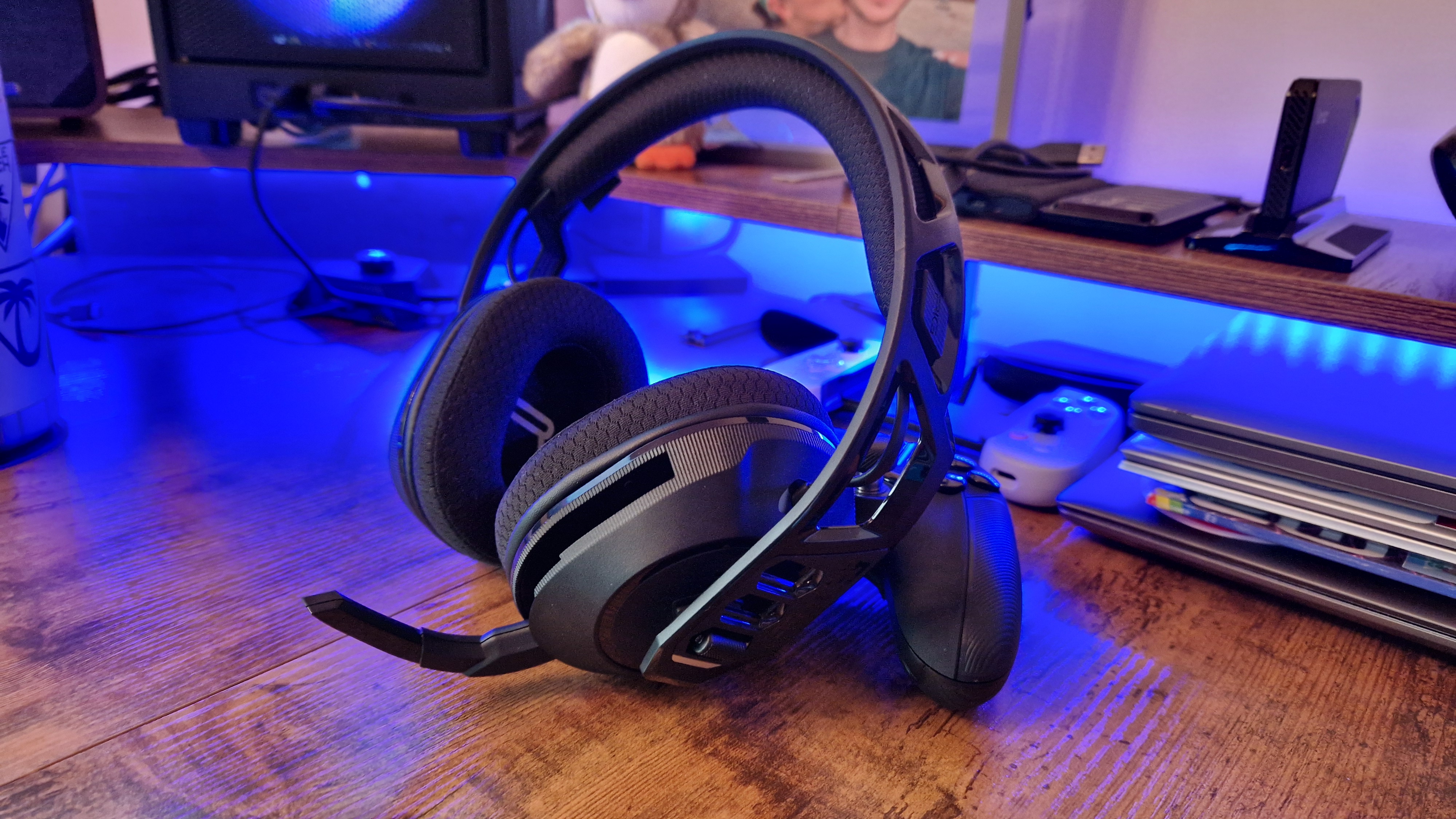 Nacon RIG 600 Pro gaming headset with its mic flipped down, propped up against a Nacon controller with blue lighting