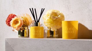 Floral Street vanilla candle and vanilla reed diffuser in yellow on side with flowers