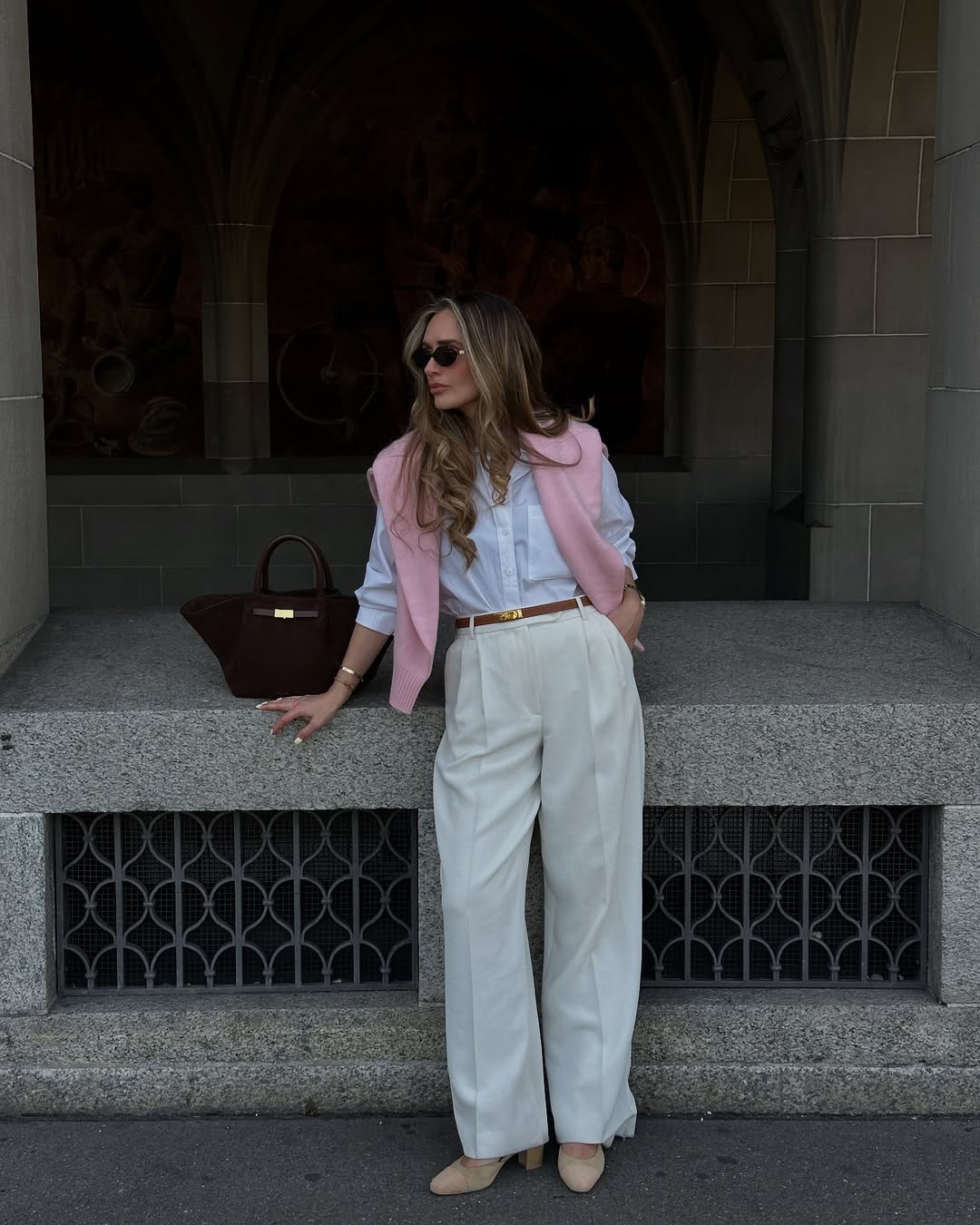 @oliviafaeh wears a pink jumper around her shoulders, a white shirt and cream trousers