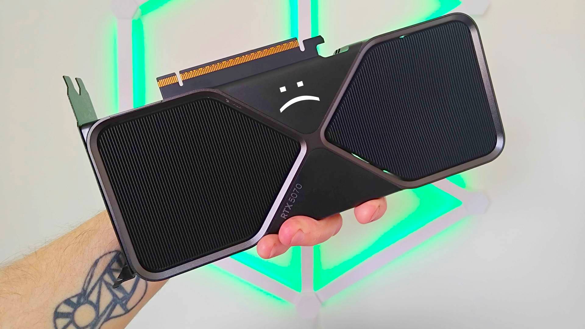 Hand holding RTX 5070 graphics card with sad text face at top.