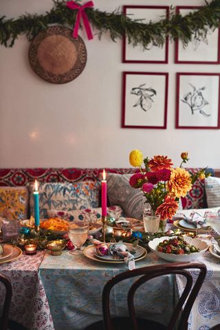 Festive Christmas table with pink and blue candles and bright floral arrangement. There are multi-patterned table cloths