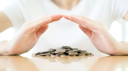 A woman holds her hands protectively over a pile of coins.