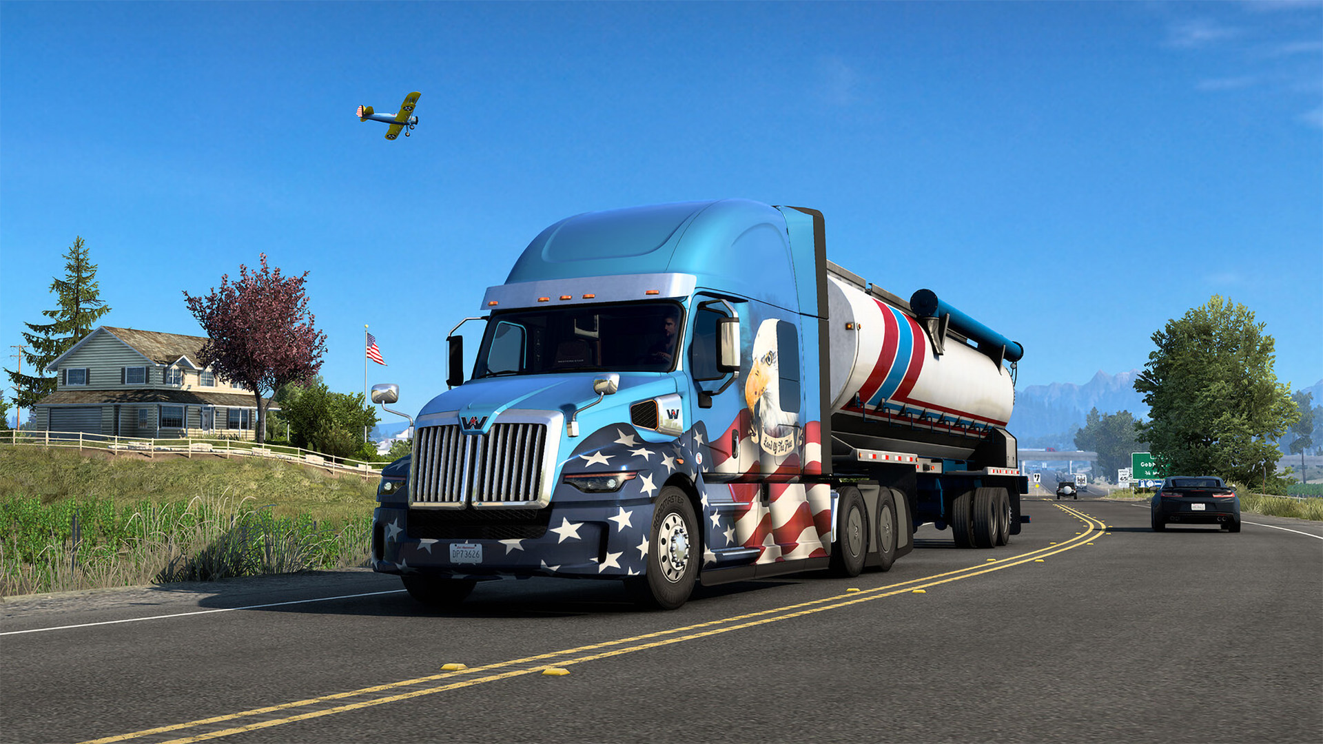A virtual semi-truck with an American flag design on a highway, with a house, car, and airplane in the gameplay scene of American Truck Simulator.