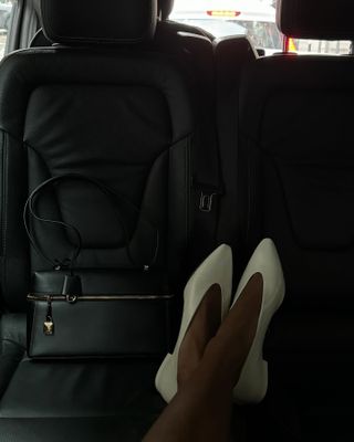 Jasmine Tookes wearing white Loro Piana almond-toe kitten heels in the back of a car.