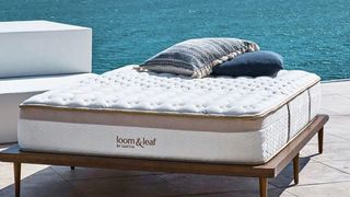 Saatva mattress sales, discounts and deals image shows the Loom & Leaf on a wooden bed frame overlooking a blue ocean