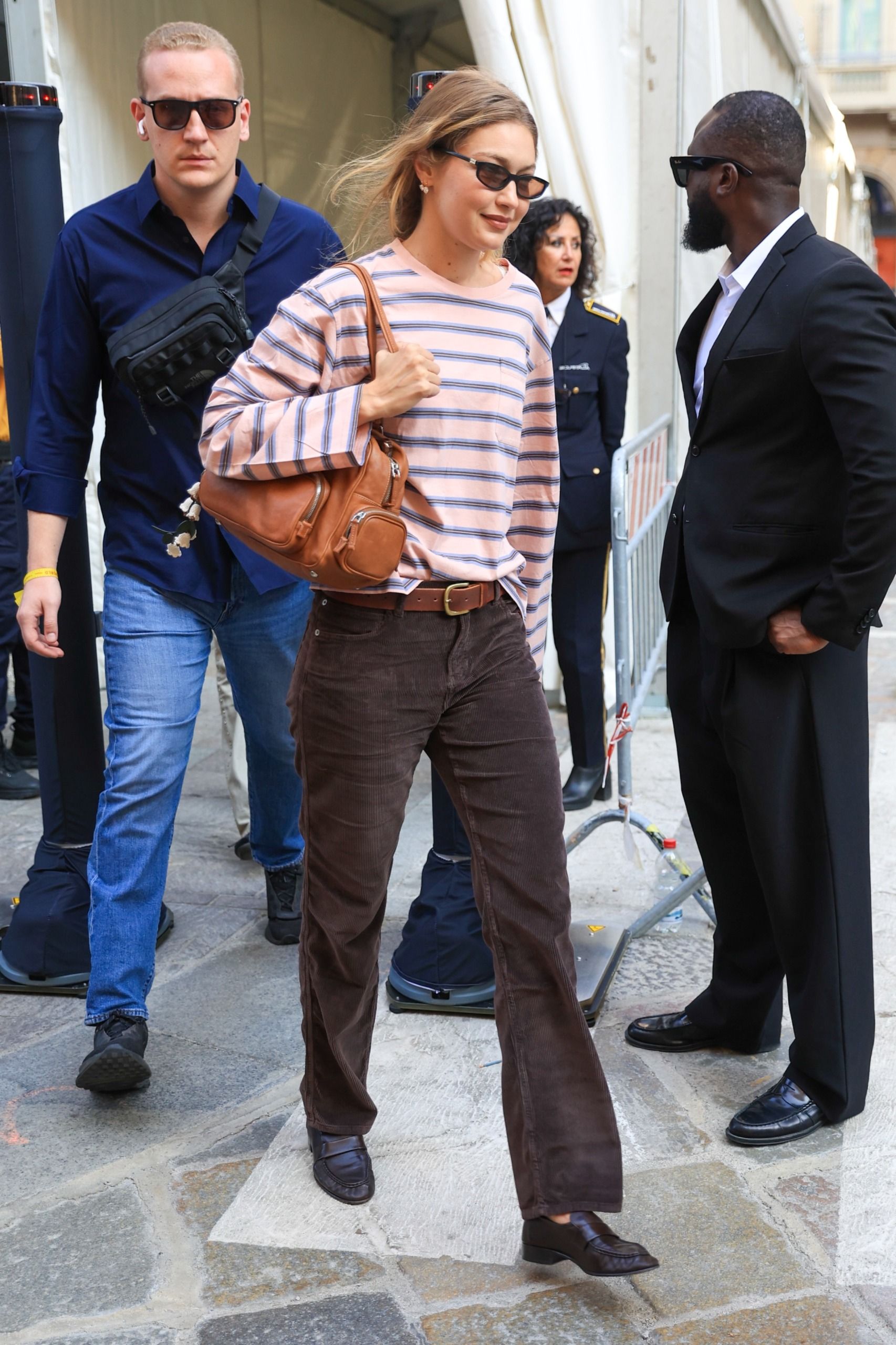 Gigi Hadid styled a striped shirt from Prada with brown corduroy bottoms, black loafers, and a Miu Miu bag at Milan Fashion Week