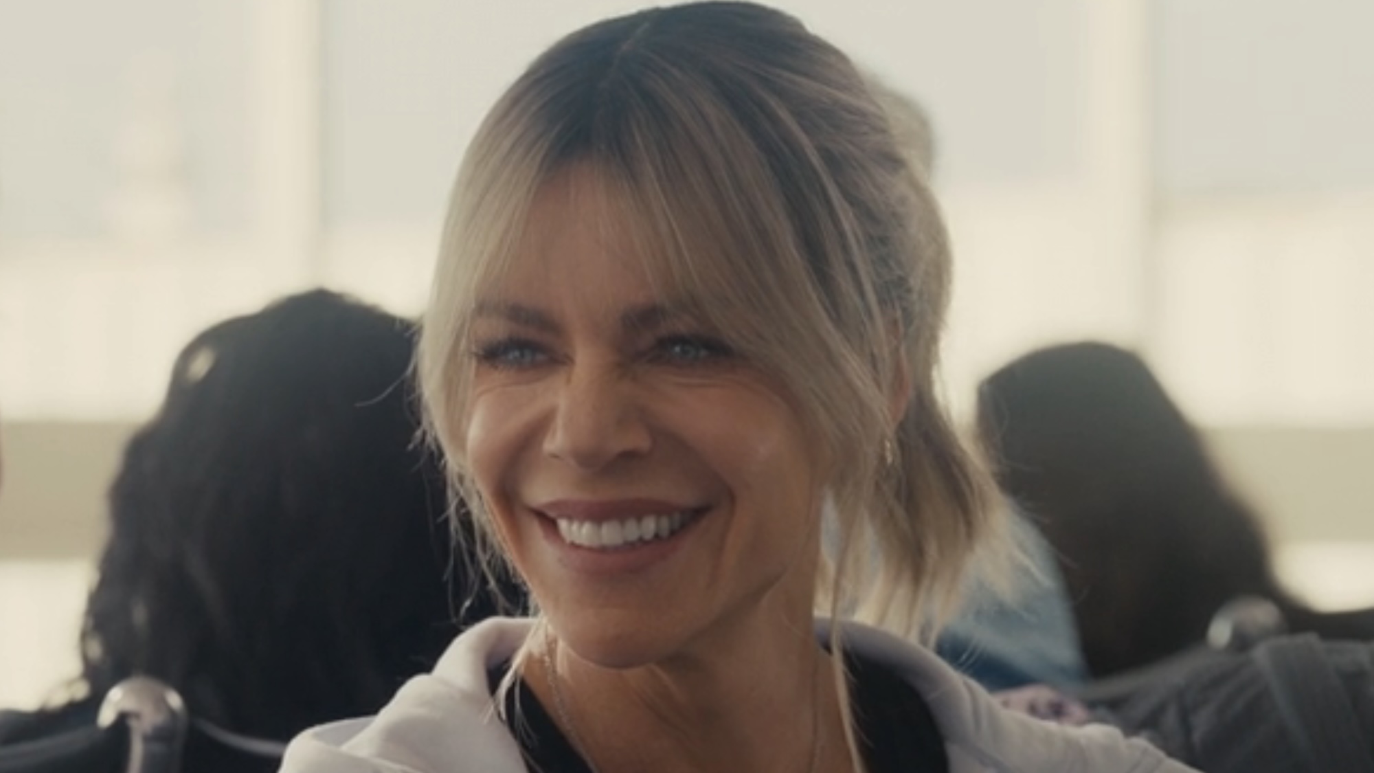 DJ smiling at Deborah sitting in airport in Hacks Season 5