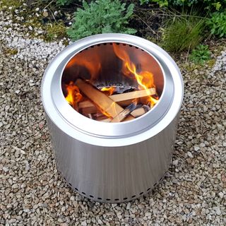 The stainless steel Solo Stove Ranger fire pit with flames coming out of the top in a gravel garden