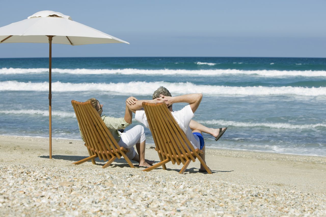 retired couple sitting in chairs at the beach.