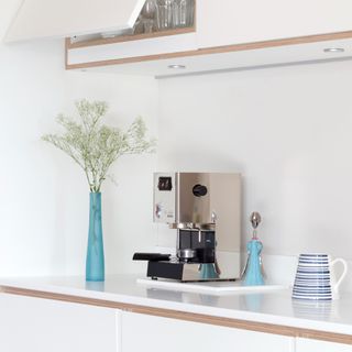 A white kitchen with a silver coffee machine and a vase of foliage